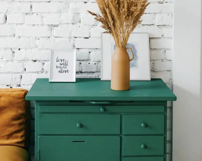 a drawer cabinet in a room, with a decorative plant and some framed photos on top of it